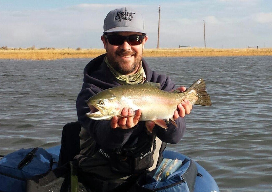 Man holding a fish on a kayak by a body of water