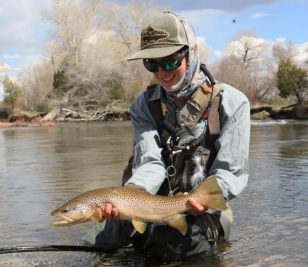 Person holding a large fish in a river with trees and sky in the background